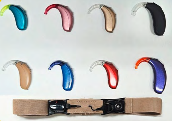 A selection of eight behind-the-ear hearing aids in various colours, arranged above a hearing aid retention strap on a white background.