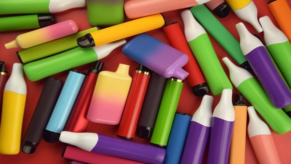 Assorted colorful glue sticks and small glue bottles scattered on a red background, typical craft supplies.