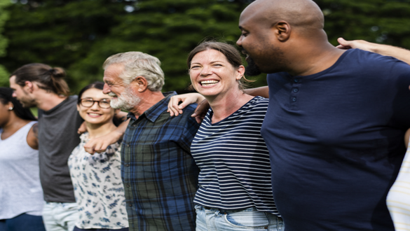 A diverse group of friends standing in a line with arms around each other, smiling outdoors in a park setting.