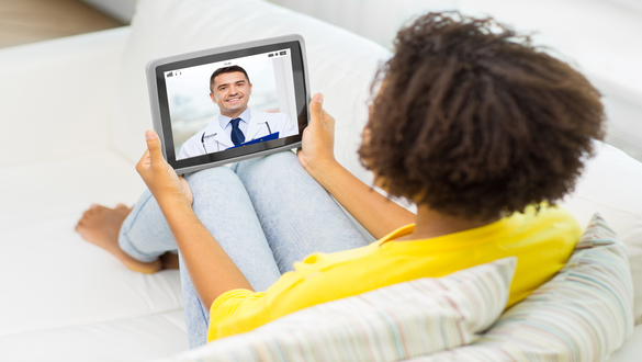 Person relaxing on a sofa while video calling a doctor on a tablet for a telemedicine appointment