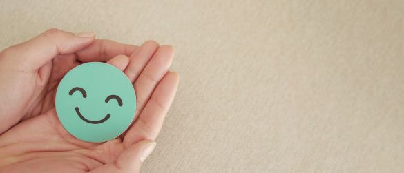 Hands cupping a mint green circular smiley-face sticker with a happy expression on a beige background.